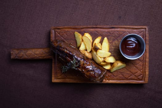 A juicy and tender beef steak is served with crispy potato wedges and a side of rosemary on a wooden board.