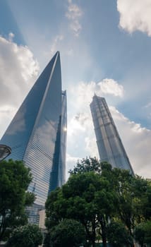 Three of Shanghais most iconic skyscrapers, including the Shanghai Tower, stand tall against a beautiful backdrop of clear blue skies and scattered white clouds.