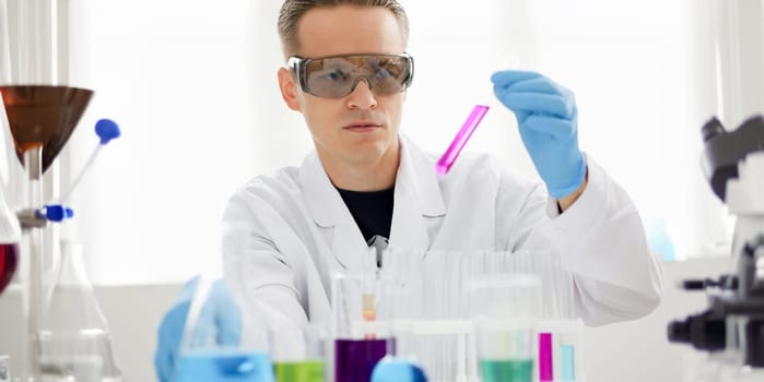 Male chemist holds test tube of glass in his hand overflows a liquid solution of potassium permanganate conducts an analysis reaction takes various versions of reagents using chemical manufacturing.