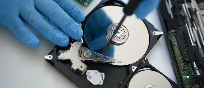 Male repairman wearing blue gloves dismantles specialized professional screwdriver hard drive. Performs fault diagnostics and performs urgent repairs recovery of lost data during deletion HDD closeup