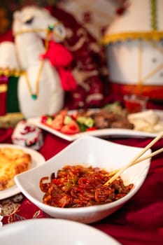 A plate of delicious noodles with meat and vegetables sits on a red tablecloth, accompanied by other dishes and a drink in the background.