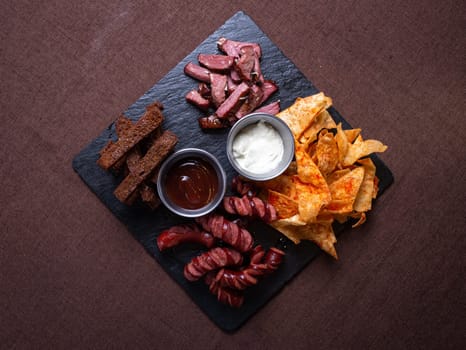 A top-down view of a tantalizing plate featuring bread, savory meat, delicious sausage, crispy chips, and flavorful dip.