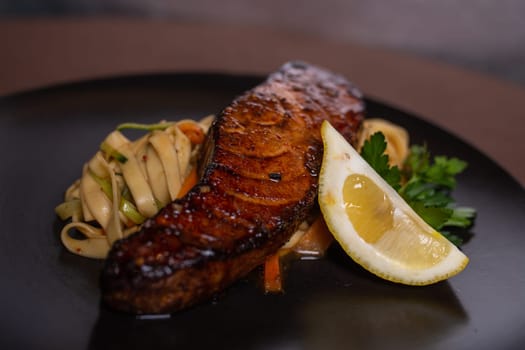 A mouthwatering and nutritious dish featuring grilled salmon, lemon, and fresh vegetables on a sleek black plate.