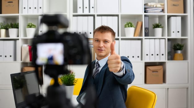 Male in suit and tie show confirm sign arm making promo videoblog or photo session in office camcorder to tripod portrait. Vlogger promotion selfie solution or finance advisor management information