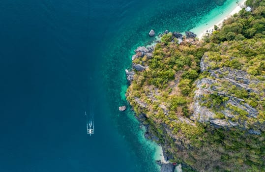 Aerial top view of a traditional philippine boat sails in sea with clear and turquoise water on the sunset.