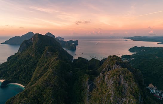 Stunning aerial view of lush, green tropical islands surrounded by calm, clear ocean waters at sunset, with a beautiful pink and orange sky. Palawan, Philippines.