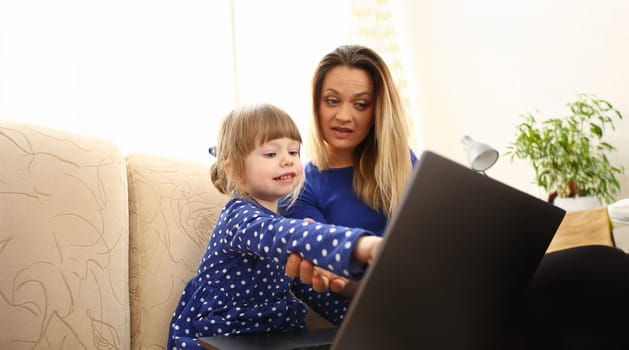 Cute little girl on couch with mom use laptop pc for chat with her dad away on business portrait. Point finger hand in display social web network bank mortgage credit wireless ip telephony concept