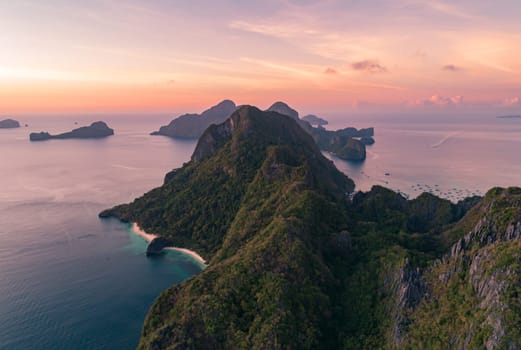 Stunning aerial view of lush, green tropical islands surrounded by calm, clear ocean waters at sunset, with a beautiful pink and orange sky. Palawan, Philippines.