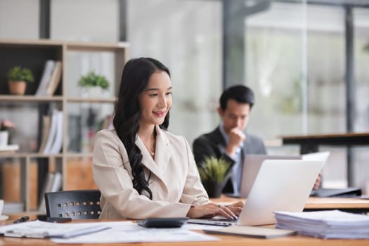 Asian businesswoman working on financial document with laptop on desk in office room.