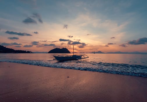 A small boat rests gently in the calm waters near a pristine beach as the sun sets.