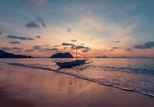 A small boat rests gently in the calm waters near a pristine beach as the sun sets.