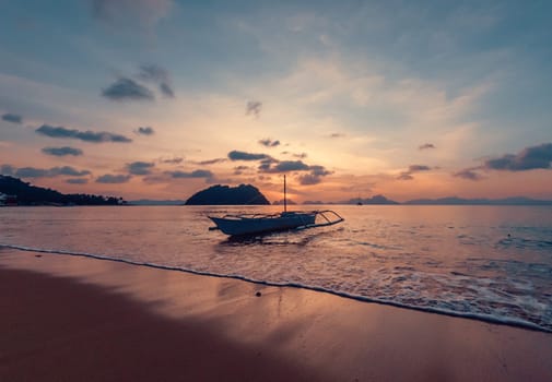 A small boat rests gently in the calm waters near a pristine beach as the sun sets.