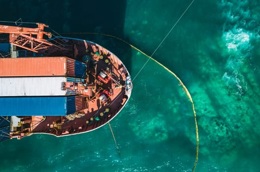 Aerial view of a container cargo ship stands aground after a storm with floating boom around the ship to prevent the spread of petroleum. Top down view of a ship bow