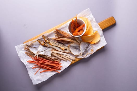 Assorted dried fish, fish skin, and fruit snacks on white paper on a wooden table, creating a vibrant culinary display.