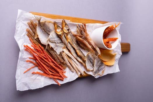 Assorted dried fish, fish skin, and fruit snacks on white paper on a wooden table, creating a vibrant culinary display.