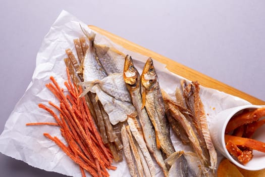 A variety of dehydrated fish, carrots, and pumpkin slices on a white paper over grey background. Isolated on a grey background.
