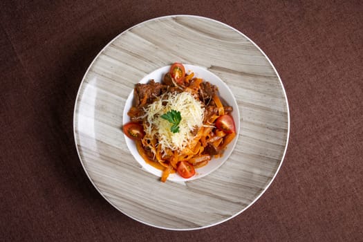Top view of a delicious plate of beef stew with pasta, tomatoes, and cheese topping, perfect for lunch or dinner.