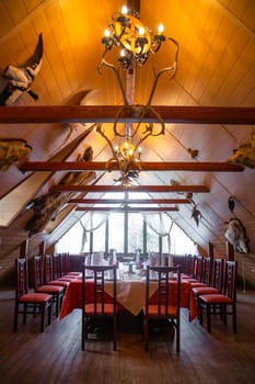 Rustic lodge interior with chandelier, red tableschairs, and mounted animal headsantlers. Ideal background for huntingnature themes.