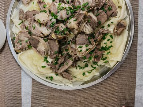 The Kazakh national dish is beshbarmak. thinly sliced beef and lamb on a large round plate with dough