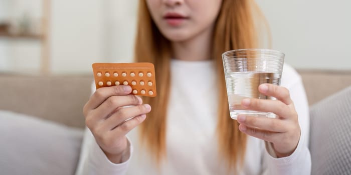 Woman holding birth control pills and a glass of water at home. Concept of health, contraception, and women's healthcare.
