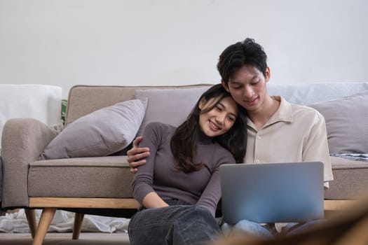 Young Asian couple in love Sitting happily together looking at laptop and relaxing in the living room. Couple making romantic love in the living room.