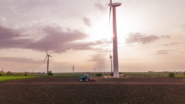 Seeds to sow. A tractor sows seeds against a background of meadows with wind turbines at sunset