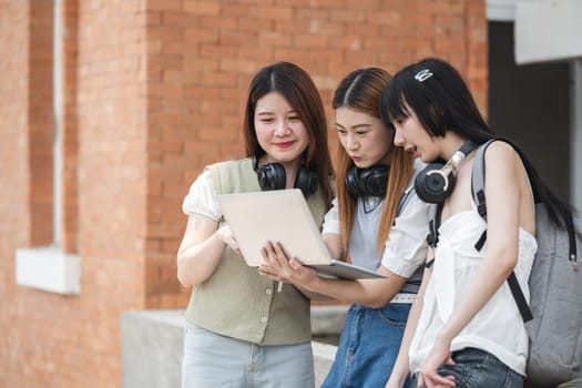 A group of female female students at an Asian university stood outside the classroom talking about their classes on laptops during break time..