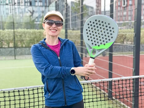 Portrait of positive young woman with racket and padel ball on tennis court. High quality photo