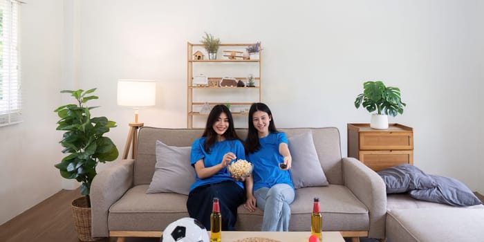 Friends watching a football game at home. Two women enjoying a sports match on TV with popcorn and snacks.