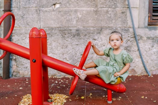 Little girl sitting on a swing balancer holding a handle on a playground. High quality photo