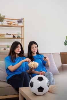 Friends watching a football game at home. Two women enjoying a sports match on TV with popcorn and snacks.