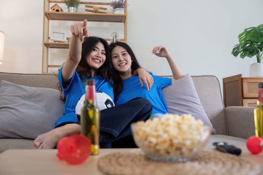Friends cheering while watching a football game at home. Two women enjoying a sports match on TV with popcorn and drinks.