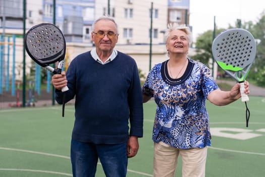 Portrait of sporty fit senior woman playing padel on open court on summer day, ready to hit ball. Health and active lifestyle concept.. High quality photo