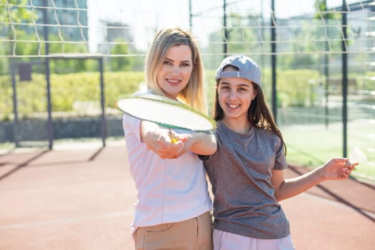 Mother and daughter are playing badminton outside in the yard on summer hot day . High quality photo