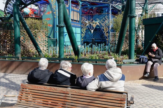 Four elderly people with gray hair are sitting and relaxing on a bench in the park. Retirement lifestyle. Copenhagen, Denmark - March 28, 2024