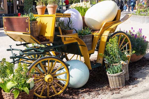 Easter decoration of a carriage with large decorative Easter eggs in a city park.