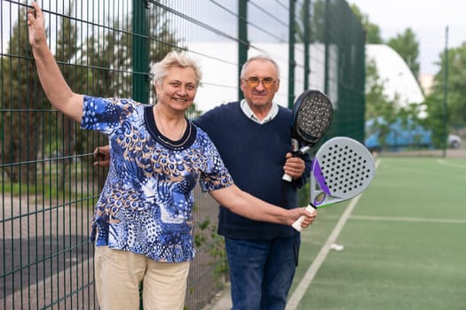 Portrait of sporty fit senior woman playing padel on open court on summer day, ready to hit ball. Health and active lifestyle concept.. High quality photo