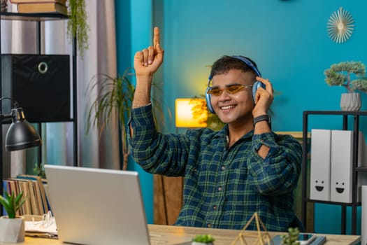 Indian man with laptop scream in delight triumph winner gesture celebrate success win money in lottery online casino game good news. Excited Hispanic guy sitting at home office workplace. Lifestyle