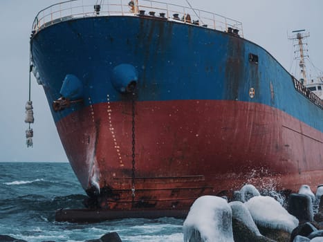 Cargo ship strands aground on a rocky shore after a storm, surrounded by snow and heavy waves.