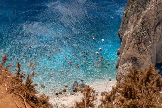 Beautiful view of a rocky beach near a cliff with floating boats in the blue sea on a sunny summer day, top view from the mountain, close-up.