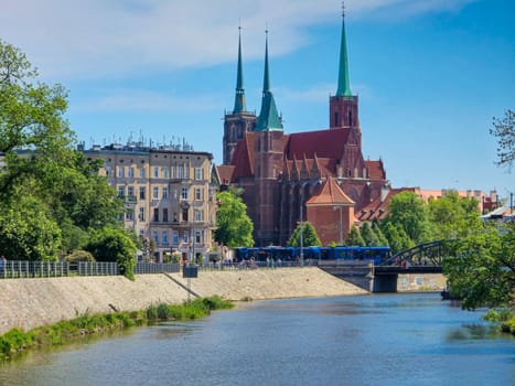 Wroclaw, Poland, 2024.05.01 - View at Tumski island and Cathedral of St John the Baptist with bridge through river Odra. Picturesque landscape spring day blue sky white cloud. High quality photo