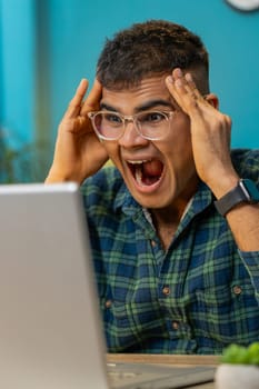 Angry Indian man having software problems with laptop angry guy nervous seeing error or mistake notification at computer screen mad employee experience virus attack or app malfunction. Vertical