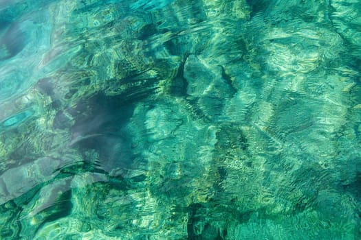 Beautiful view of emerald-colored water with a stone bottom in the sea on a sunny summer day, close-up view from above.