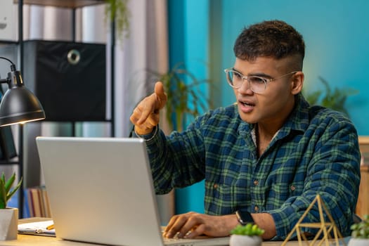 Quarrel. Furious annoyed businessman freelancer engage in heated laptop conversations at home office. Upset boss expresses frustration using cellphone Indian manager guy disputes with subordinates