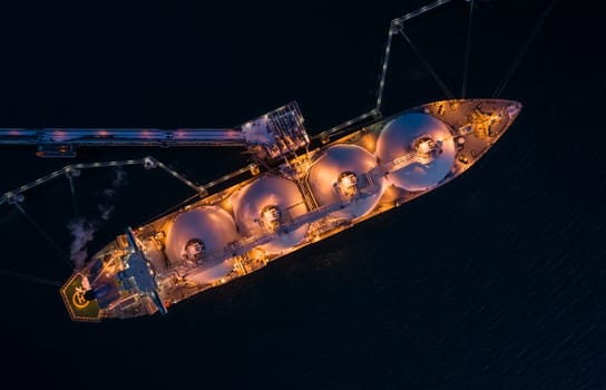 Aerial of Liquified Natural Gas LNG carrier moored to a small gas terminal at night. Fuel crisis. Sanctions. Top down shot.