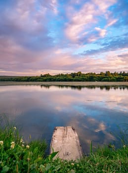 A serene countryside scene during sunset, showcasing a tranquil lake with a wooden dock in the foreground.