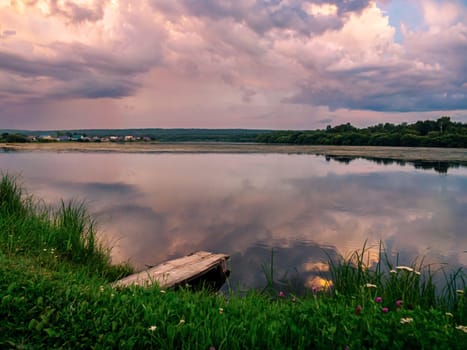 A serene countryside scene during sunset, showcasing a tranquil lake with a wooden dock in the foreground.