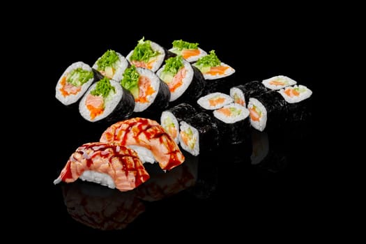Collection of maki rolls and nigiri sushi with salmon and vegetable fillings drizzled with unagi sauce, displayed on reflective black surface, emphasizing rich colors and textures of Japanese cuisine