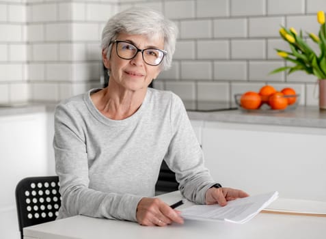 Woman With Grey Hair Is At Home, Sitting At Table With Documents