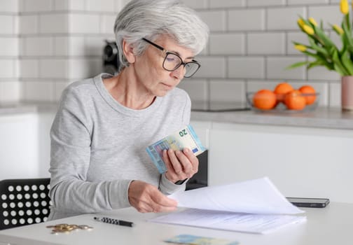 Elderly Woman At Home Holds Euro Money And Examines Documents